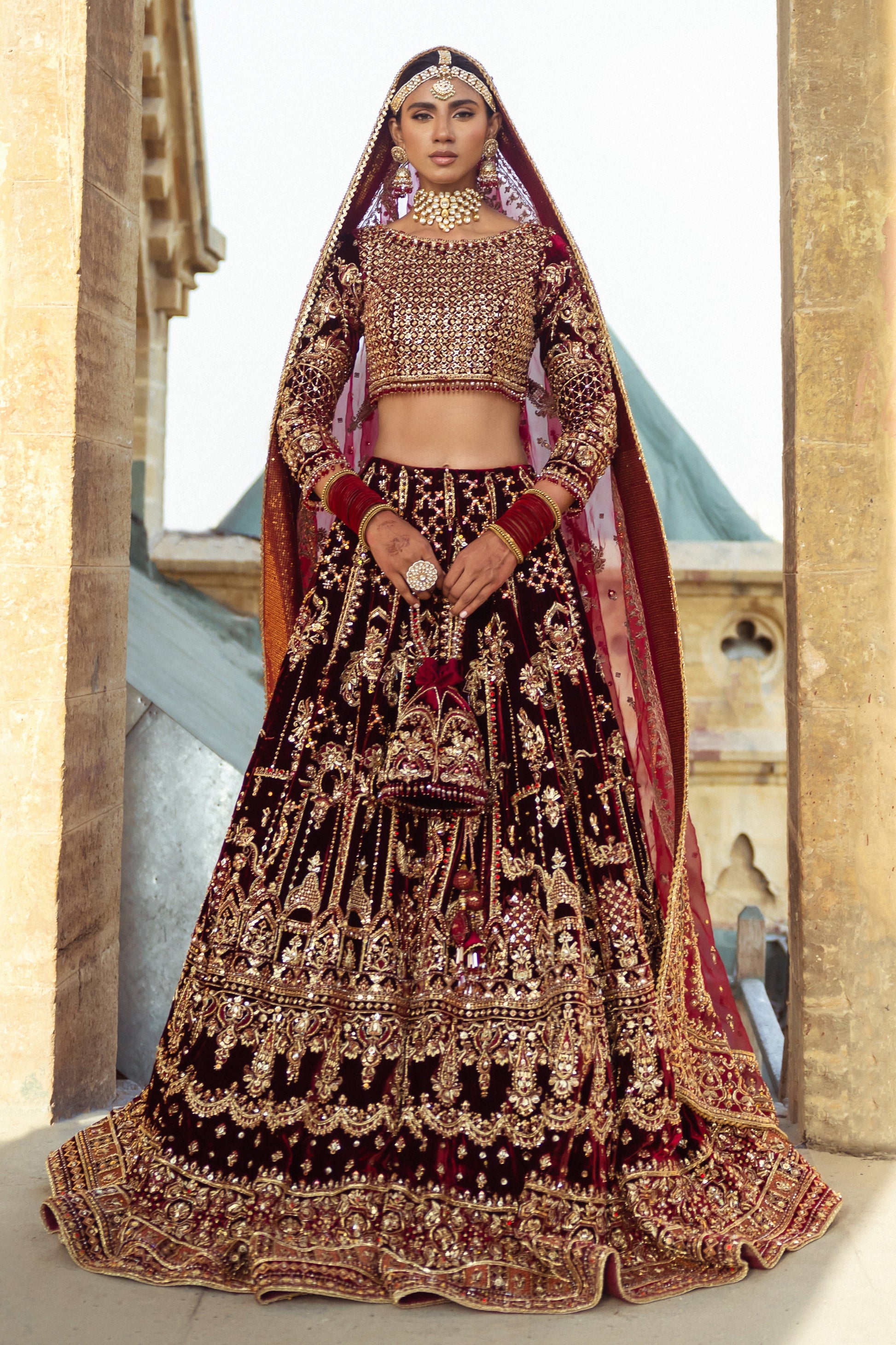 Parivarsh dark maroon velvet bridal lehenga choli by NAQSHI, full front view with heavily embellished choli, flared velvet lehenga, organza dupatta and matching potli bag, ready to wear 4-piece barat wedding outfit.