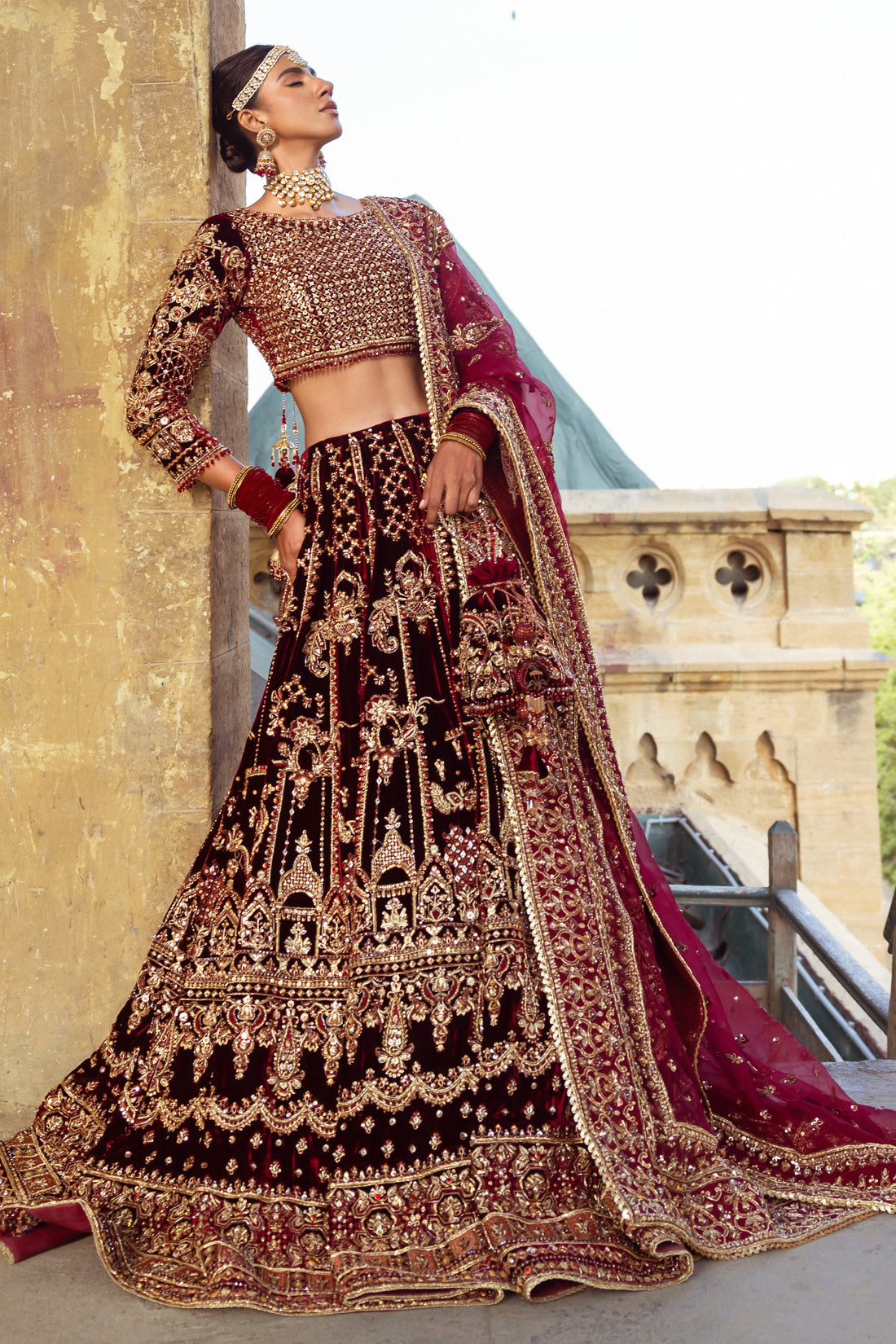 Parivarsh dark maroon velvet bridal lehenga choli by NAQSHI, full front view with heavily embellished choli, flared velvet lehenga, organza dupatta and matching potli bag, ready to wear 4-piece barat wedding outfit.