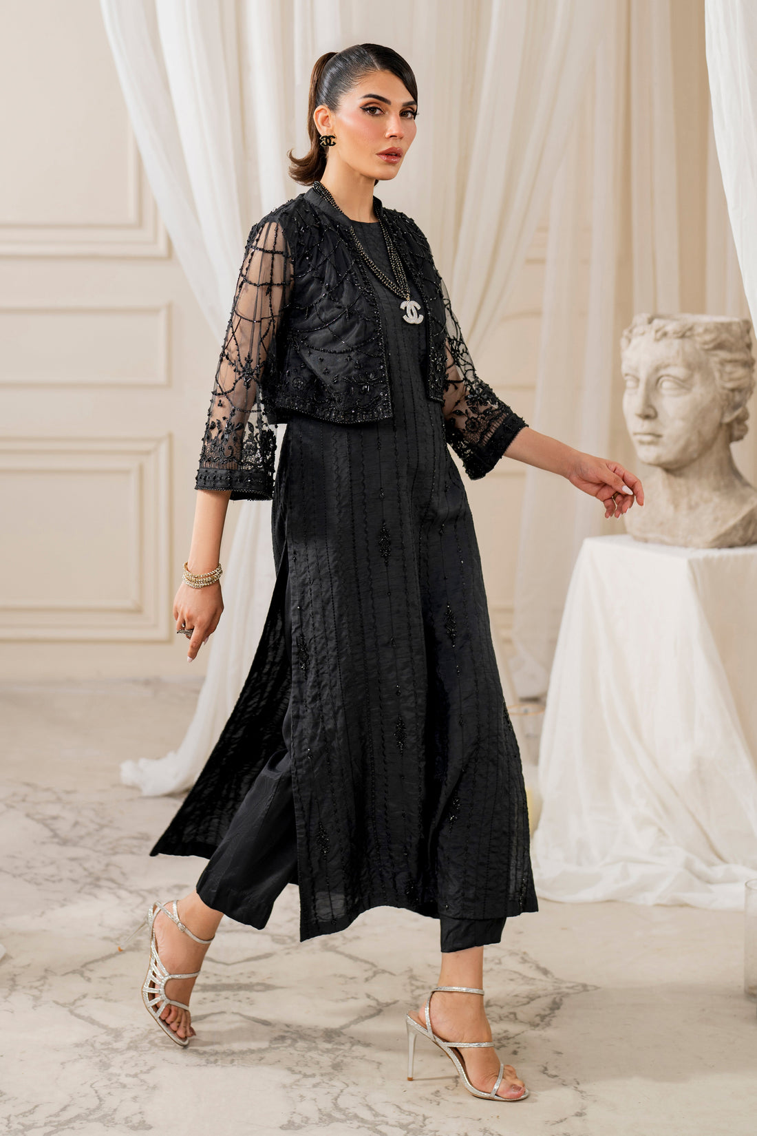 Naqshi siara black raw‑silk straight shirt with matching geometic embroidered net cropped jacket, crystal and bead hangings, paired with straight pants and sequin dupatta.