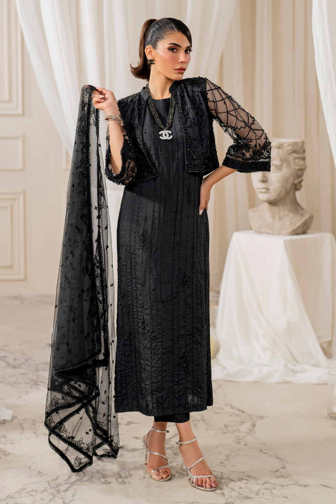 Naqshi siara black raw‑silk straight shirt with matching geometic embroidered net cropped jacket, crystal and bead hangings, paired with straight pants and sequin dupatta.