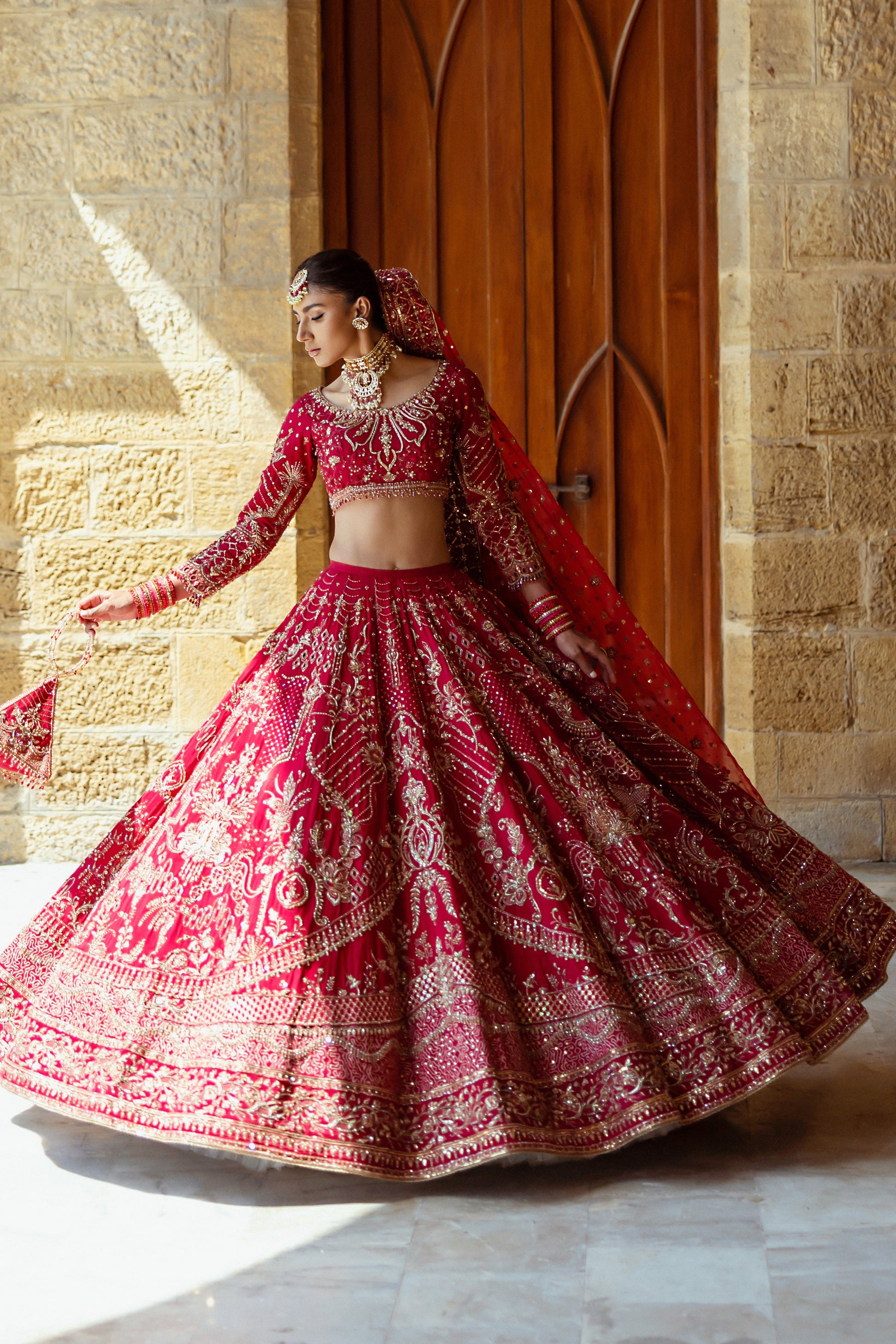 Twirl pose of Qurbat fuchsia red bridal lehenga showing circular flare and detailed borders, elegant barat wedding outfit.