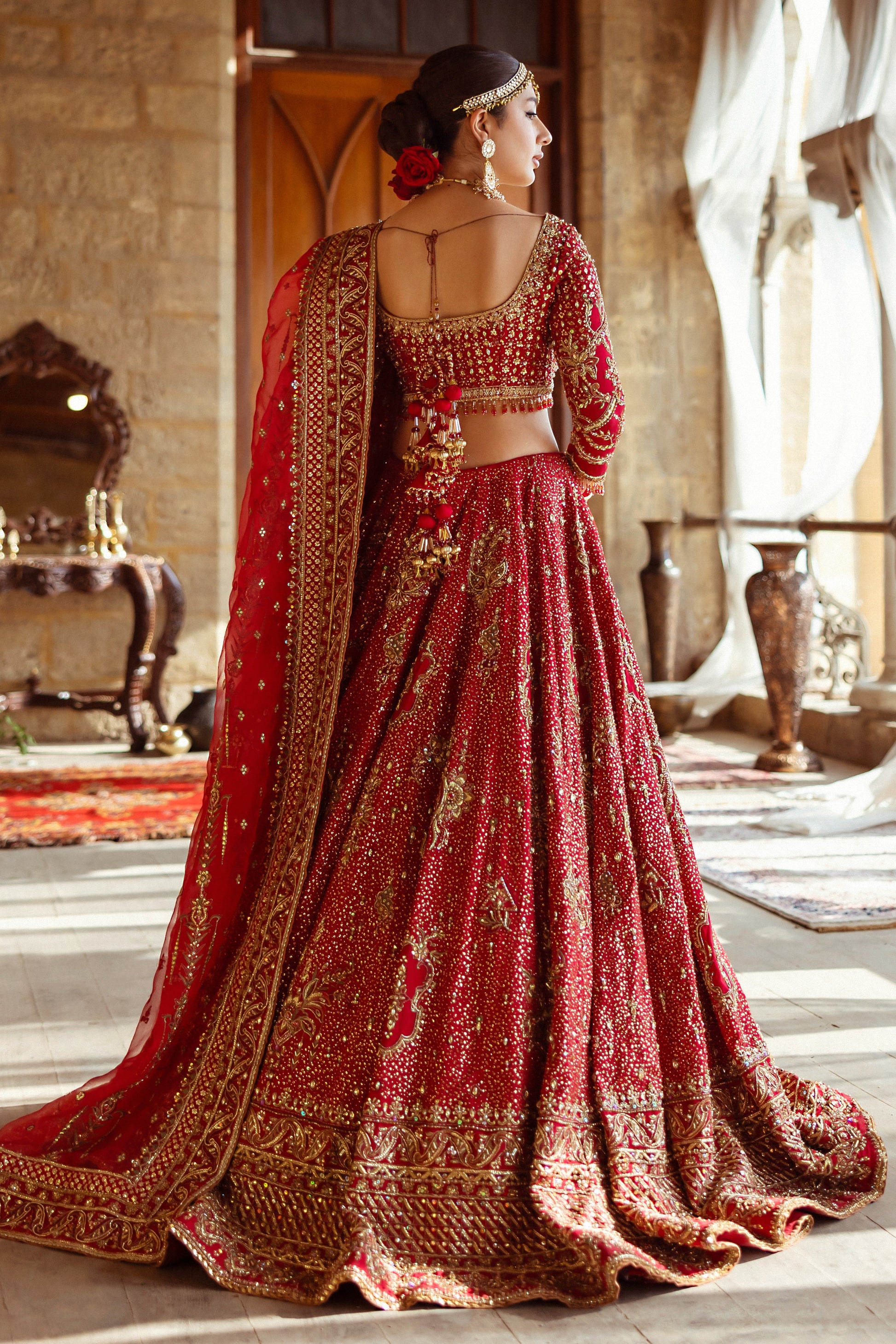 Side profile of NAQSHI Shahana showing voluminous lehenga flare, texture-play on panels, scalloped sleeve detailing, crystal hangings and structured dupatta drape