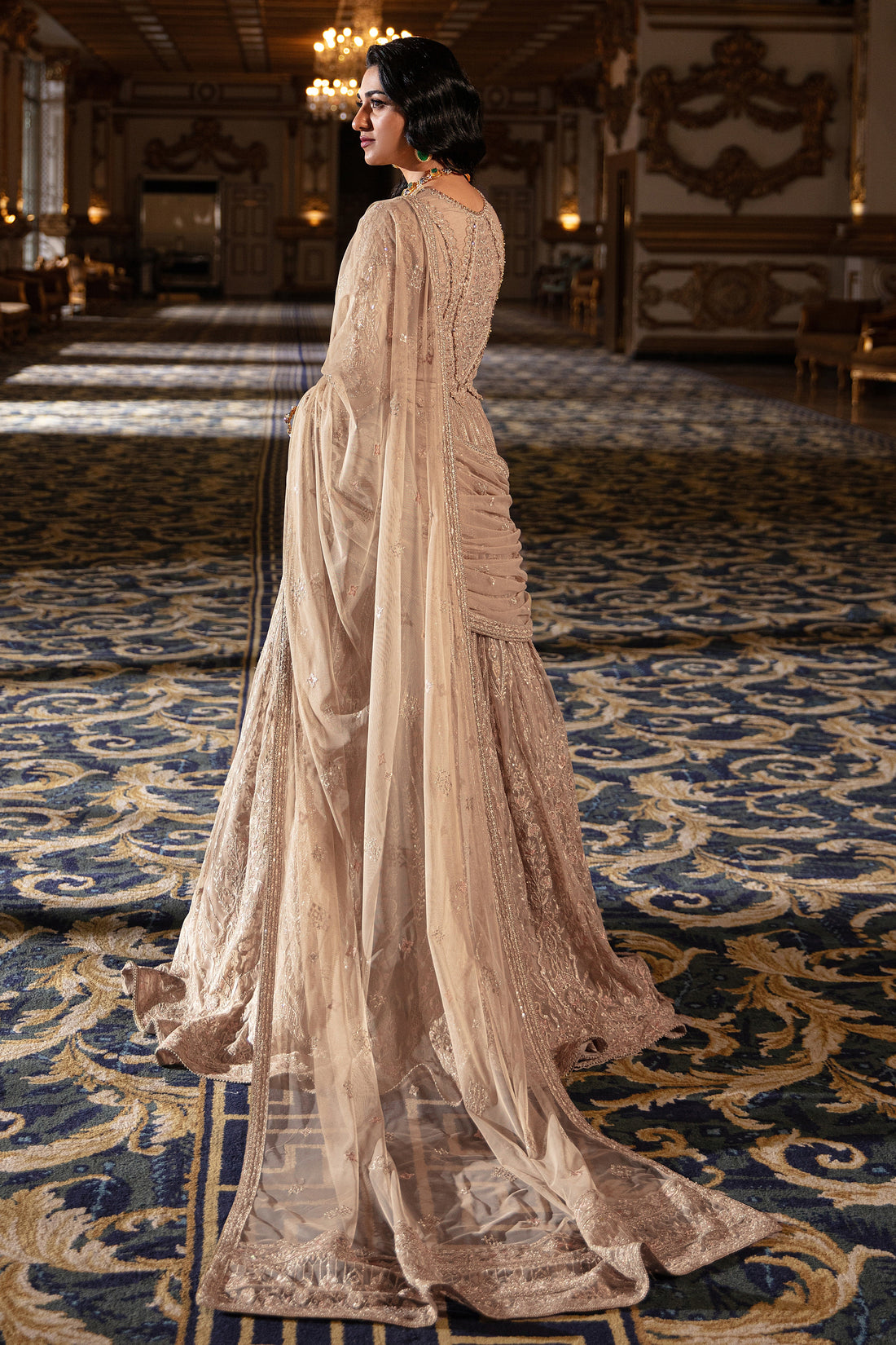 Naqshi Areeza skin‑gold net choli richly embroidered with hand‑adda motifs, sequin detailing, scalloped sleeves with dangling tassels, paired with voluminous lehanga.