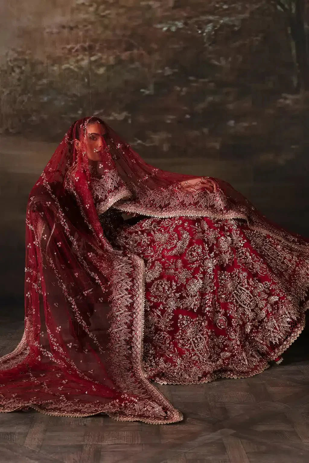 Model seated with veil over head wearing Afrozeh The Brides Edit 23 Adelaide bridal dress in brick red net with ornate gold embroidery and long train.