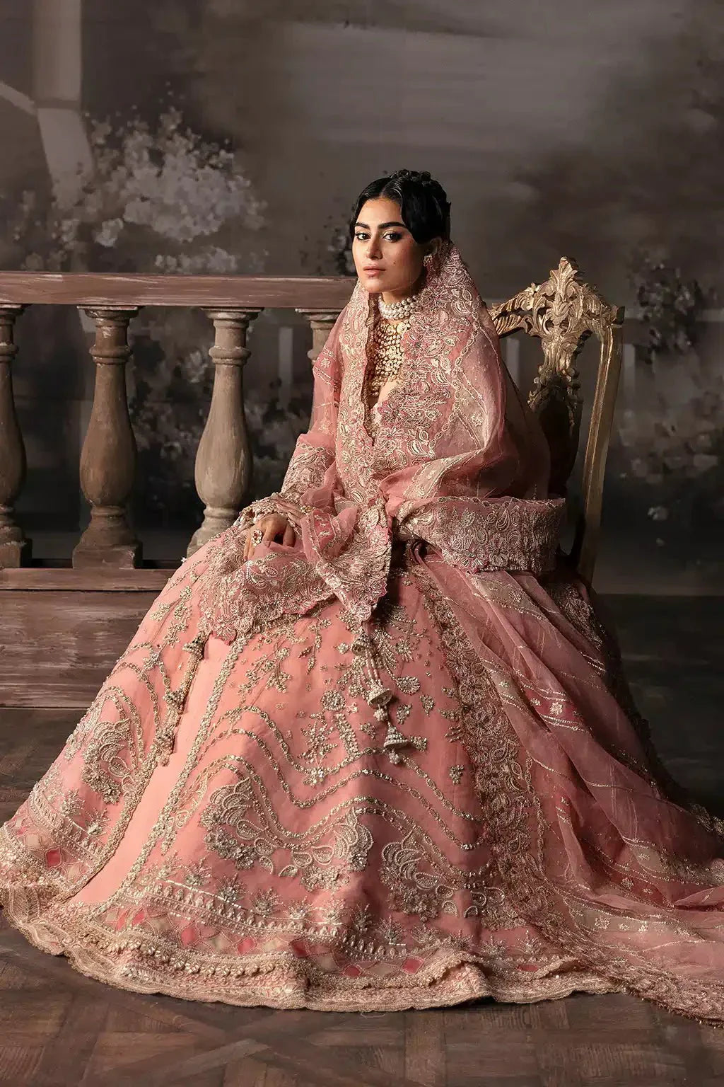 Seated model in Afrozeh The Brides Edit 23 Victoria bridal dress, highlighting the luxurious embroidery and regal tea pink organza fabric.