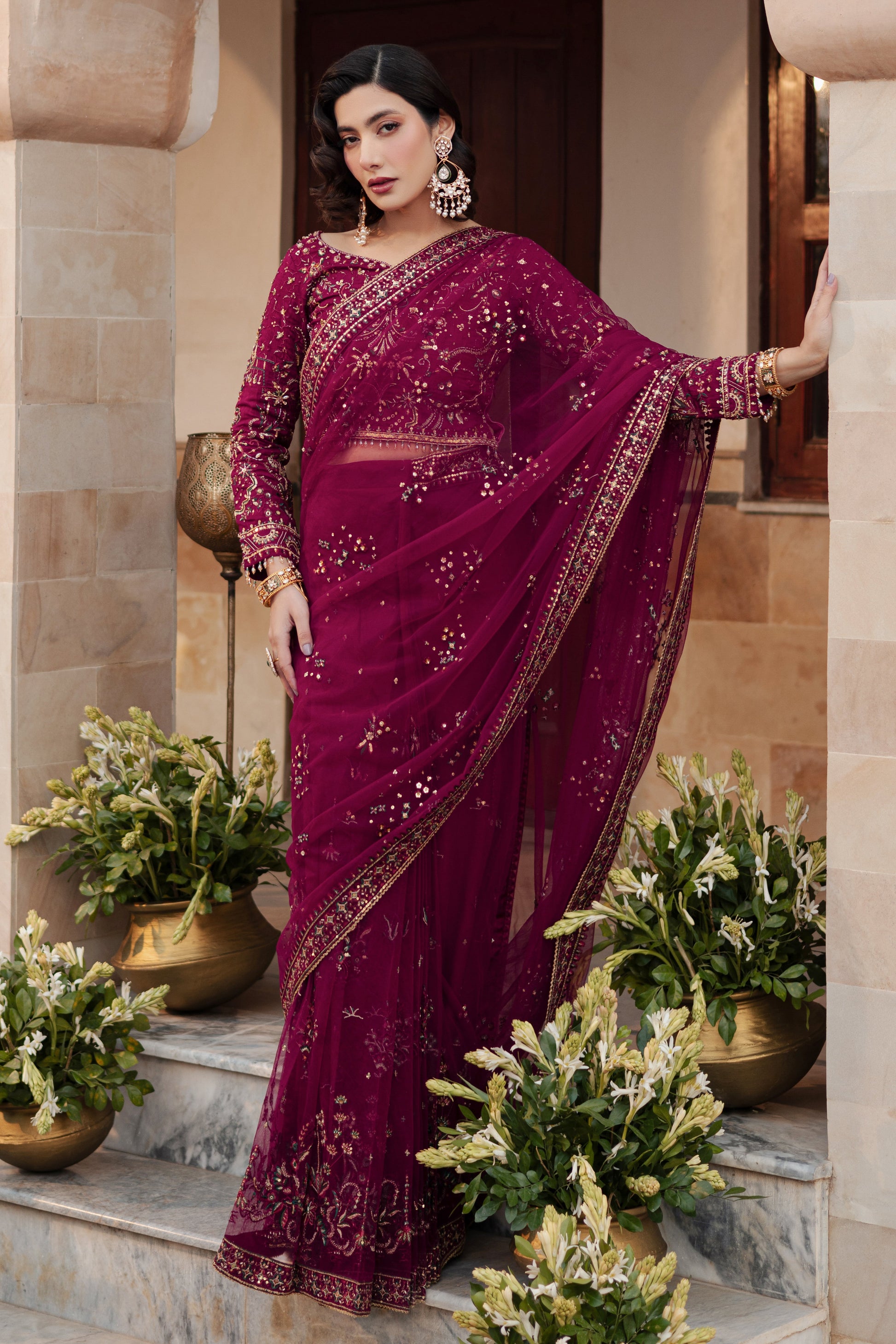 Styled NAQSHI Meeru ensemble: burgundy net saree with embroidered blouse and raw silk petticoat, expertly draped for an elegant formal occasion